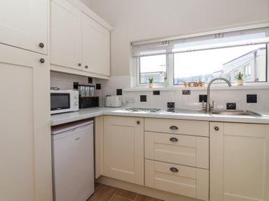 A kitchen with white cabinets a microwave toaster sink and window with decorative items at Atlantic Escape in Widemouth Bay