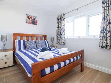 A bedroom with a wooden bed with blue and white striped bedding and patterned pillows at Atlantic Escape in Widemouth Bay