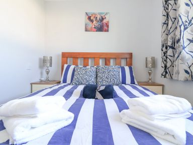 A bedroom with a wooden bed frame striped blue and white bedding pillows bedside tables with lamps and folded white towels on the bed at Atlantic Escape in Widemouth Bay