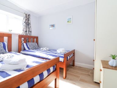 A bedroom with two single wooden beds with blue and white striped bedding at Atlantic Escape in Widemouth Bay