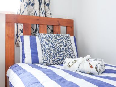 A single bed with blue and white striped bedding a leaf patterned pillow and a rolled blanket on top at Atlantic Escape in Widemouth Bay