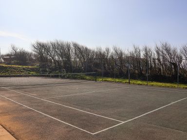 An outdoor tennis court with a net and bare trees in the background at Atlantic Escape in Widemouth Bay