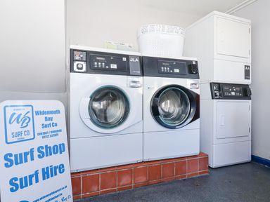 A laundry room with washing machines dryer and a surf shop sign at Atlantic Escape in Widemouth Bay