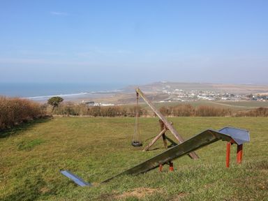 A playground with a metal slide and a hanging tire swing overlooking a coastal village and the sea at Atlantic Escape in Widemouth Bay