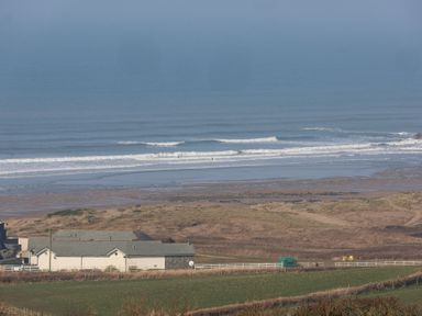 A coastal scene with a house near grassy fields and waves on the beach at Atlantic Escape in Widemouth Bay
