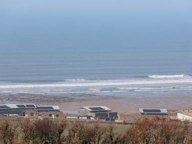 A coastal view with modern buildings near the beach and ocean waves at Atlantic Escape in Widemouth Bay