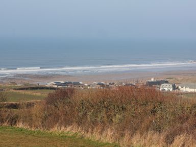 A coastal view with fields bushes buildings and a beach at Atlantic Escape in Widemouth Bay