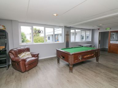 A game room with a pool table a leather armchair and windows showing an open sign at Atlantic Escape in Widemouth Bay