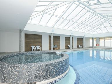 An indoor swimming pool with a circular hot tub and plastic chairs at Atlantic Escape in Widemouth Bay