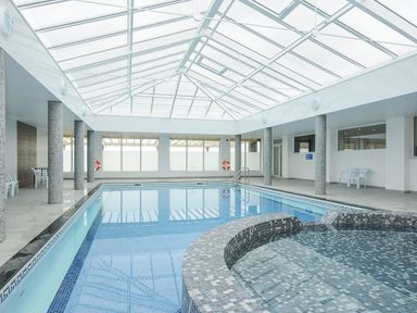 An indoor swimming pool with a hot tub under a glass roof at Atlantic Escape in Widemouth Bay