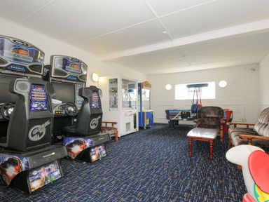 A game room with arcade racing machines a claw machine air hockey table and upholstered chairs at Atlantic Escape in Widemouth Bay