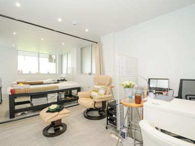 A treatment room with a massage table armchair footstool and desk with chair at Atlantic Escape in Widemouth Bay