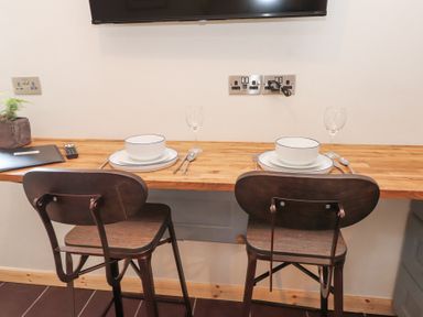 A wooden countertop with two place settings and two dark wooden chairs at Cwt Mochyn in Llanberis