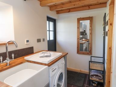 A utility room with a sink washing machine mirror and shelving at Cwt Mochyn in Llanberis
