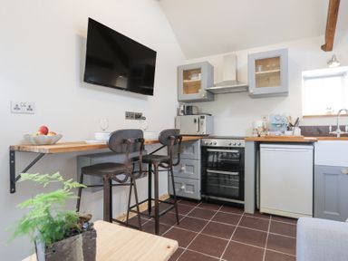 A kitchen with gray cabinets a wooden countertop a wall-mounted television and two high chairs at Cwt Mochyn in Llanberis