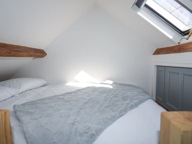 A bedroom with a bed covered with white linens and a grey blanket under a slanted ceiling with wooden beams and a skylight window at Cwt Mochyn in Llanberis