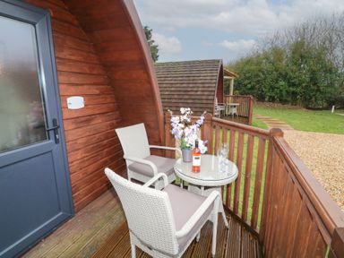A wooden porch with two white chairs and a round table holding flowers and a bottle of wine at Chantelles in Holbeach