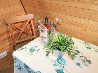 A table with a floral tablecloth a metal bucket with a bottle and wine glasses and a potted plant beside a wooden chair and wood paneled walls at Chantelles in Holbeach