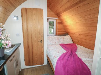 A small bedroom with wooden walls a bed with floral bedding and a pink blanket next to a kitchenette at Chantelles in Holbeach