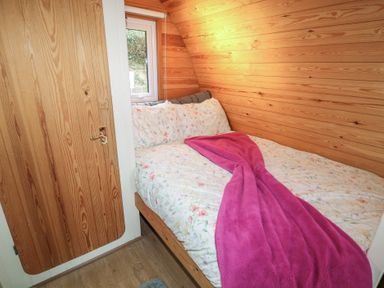 A small bedroom with wooden walls a bed with floral bedding and a pink blanket at Chantelles in Holbeach