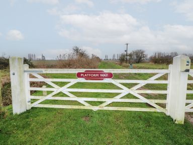A white wooden gate with a platform way sign on a grassy rural path at Chantelles in Holbeach