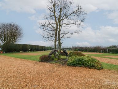 A gravel pathway with trimmed hedges a leafless tree and two deer statues at Chantelles in Holbeach