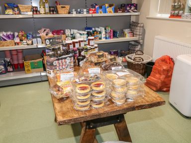 A display table with packaged cakes jams and crackers near shelves with toiletries and food items at Charlottes in Holbeach