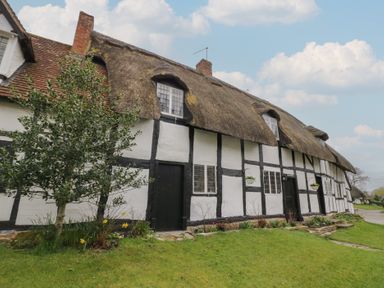 A traditional thatched cottage with white walls black timber framing and a garden with flowers at Church View in Welford-On-Avon