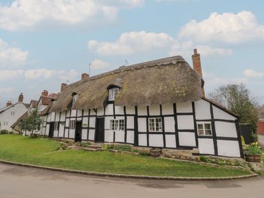 A thatched roof cottage with white walls and black timber framing beside a road at Church View in Welford-On-Avon