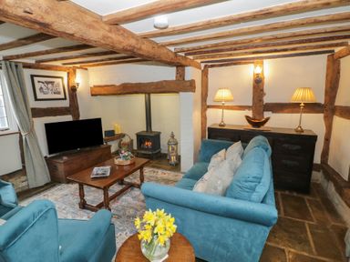 A living room with wooden beams a blue sofa two armchairs a wooden coffee table a fireplace and a television at Church View in Welford-On-Avon