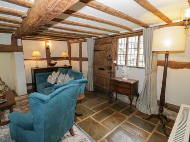A living room with wooden beams stone floor and blue upholstered chairs at Church View in Welford-On-Avon