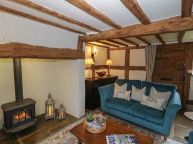 A living room with a blue sofa a wooden coffee table a fireplace and wooden beams at Church View in Welford-On-Avon