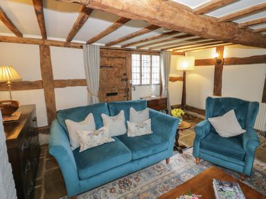 A sitting room with blue upholstered sofa and armchair wooden beams on ceiling and walls at Church View in Welford-On-Avon