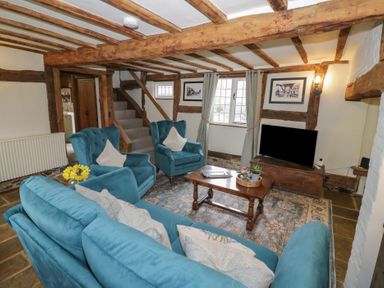 A living room with blue upholstered chairs and sofa a wooden coffee table and a television at Church View in Welford-On-Avon