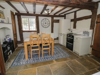 A kitchen dining area with wooden beams a wooden table and chairs a rug a refrigerator oven and cabinets at Church View in Welford-On-Avon