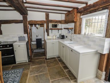 A kitchen with stone tile floor wooden ceiling beams white cabinets and a sink under a window at Church View in Welford-On-Avon
