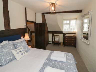 A bedroom with a bed a lamp a chair a chest of drawers and a mirror at Church View in Welford-On-Avon