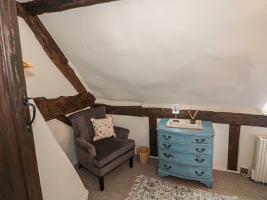 An armchair with a heart patterned cushion next to a blue chest of drawers with a lamp and diffuser on top at Church View in Welford-On-Avon