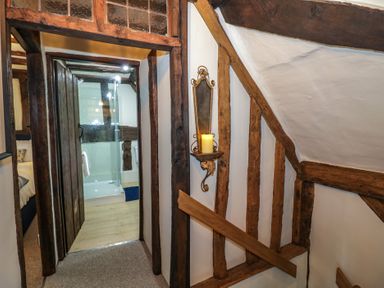 A hallway with wooden beams and a candle holder on the wall leading to a bathroom with a glass shower at Church View in Welford-On-Avon