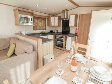 A kitchen and dining area with a table set with plates and glasses next to a sofa at Lodge 1 in Silverdale