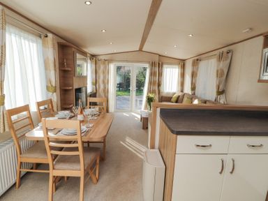 A dining area with a wooden table set for four and a living room with a sofa and coffee table at Lodge 1 in Silverdale