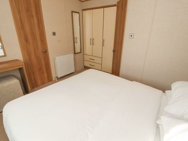 A bedroom with a bed a wardrobe a radiator two wooden doors and a dressing table at Lodge 1 in Silverdale