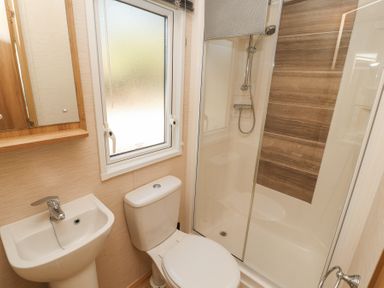 A small bathroom with a sink toilet window and shower with wooden wall panels at Lodge 1 in Silverdale