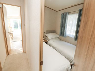 A small bedroom with two single beds and a window with blue curtains at Lodge 1 in Silverdale