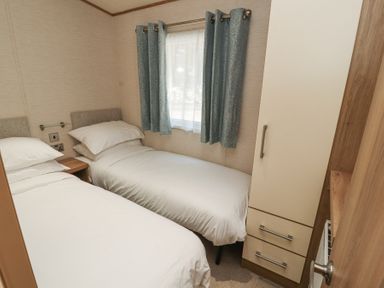 A small bedroom with two single beds a window with blue curtains and a wardrobe at Lodge 1 in Silverdale