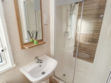 A bathroom with a sink and mirror and a glass-enclosed shower with brown tiled wall at Lodge 1 in Silverdale