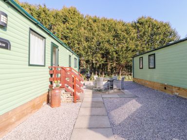 An outdoor area between two green mobile homes with a patio table and chairs and a charcoal barbecue grill at Lodge 1 in Silverdale