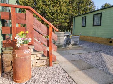 An outdoor patio area with wooden stairs a rusty milk can with flowers and a table with chairs at Lodge 1 in Silverdale