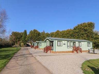 A row of light green lodges with wooden steps along a gravel driveway surrounded by trees at Lodge 1 Silverdale