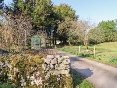 A country road leading past a stone wall and a sign reading old waterslack farm with trees and a fence alongside at Lodge 1 in Silverdale